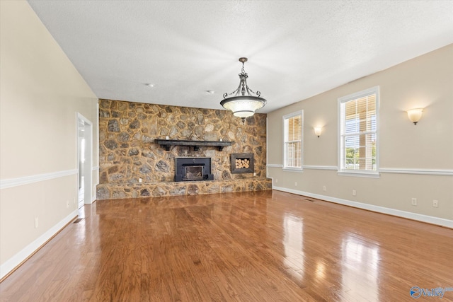 unfurnished living room with a textured ceiling, a stone fireplace, wood finished floors, and baseboards