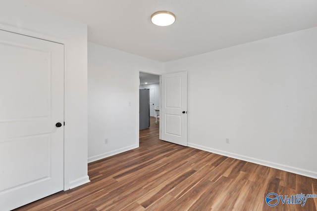 unfurnished bedroom featuring dark hardwood / wood-style floors and stainless steel refrigerator