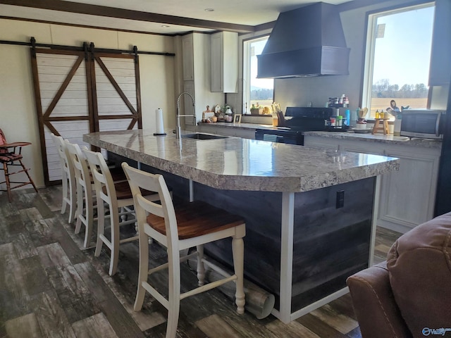 kitchen featuring dark wood-type flooring, ventilation hood, a breakfast bar, a sink, and electric stove