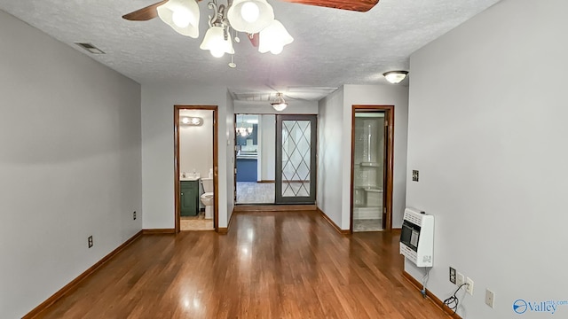 interior space with a textured ceiling, ceiling fan, heating unit, and hardwood / wood-style flooring