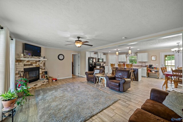 living room with ornamental molding, ceiling fan with notable chandelier, a stone fireplace, and a textured ceiling