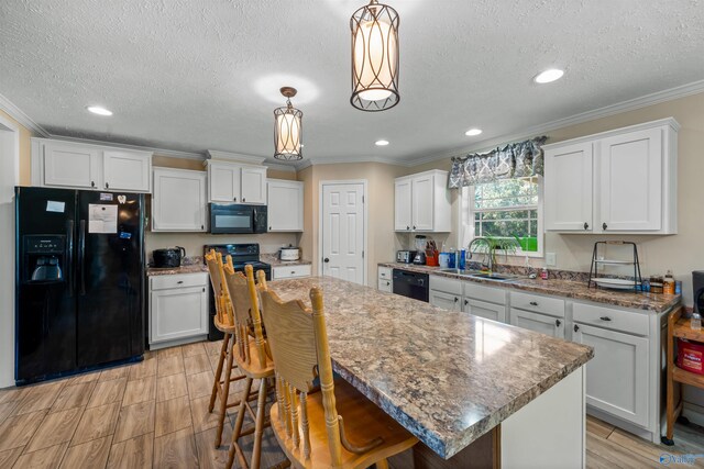 kitchen with white cabinetry, black appliances, hanging light fixtures, crown molding, and a center island