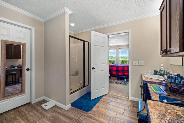 bathroom with a textured ceiling, ornamental molding, vanity, and an enclosed shower