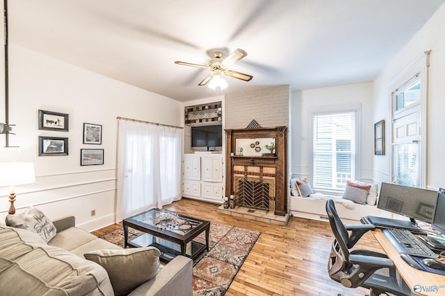 living room featuring a brick fireplace, light wood-style flooring, and a ceiling fan