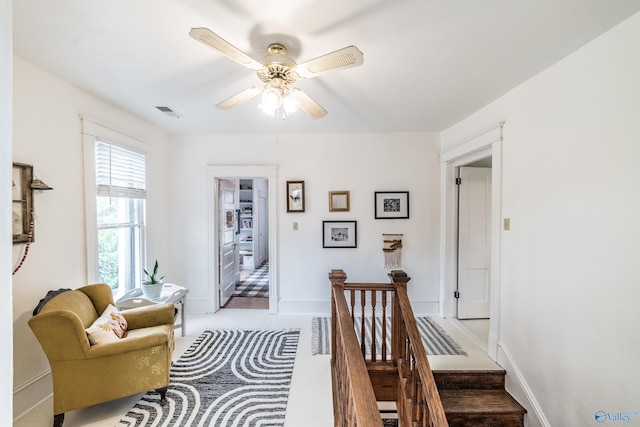 living area featuring a ceiling fan, an upstairs landing, and baseboards