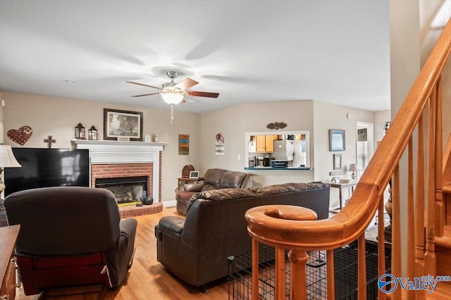 living room featuring light hardwood / wood-style floors, ceiling fan, and a brick fireplace