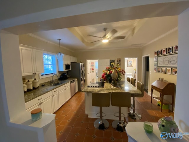 kitchen with a breakfast bar, a sink, appliances with stainless steel finishes, a raised ceiling, and crown molding