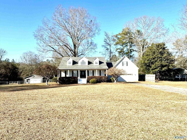 cape cod house with covered porch, an outbuilding, a garage, and a front yard