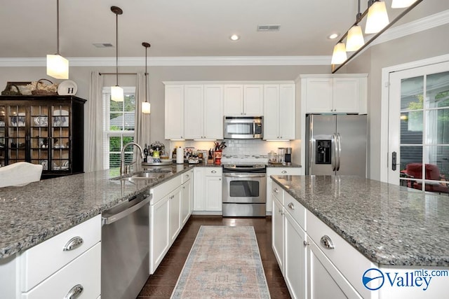 kitchen with appliances with stainless steel finishes, dark stone counters, white cabinetry, and decorative light fixtures