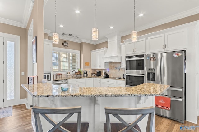 kitchen with premium range hood, backsplash, a breakfast bar, white cabinets, and appliances with stainless steel finishes