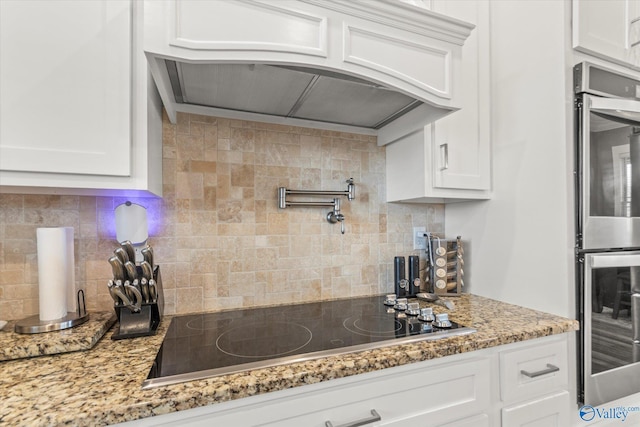 kitchen featuring decorative backsplash, black electric stovetop, white cabinets, and light stone counters