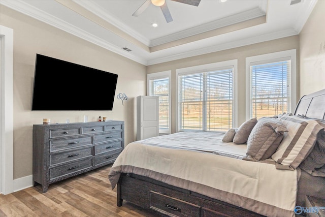 bedroom featuring ceiling fan, light hardwood / wood-style floors, ornamental molding, and a tray ceiling