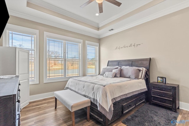 bedroom featuring a tray ceiling, multiple windows, ceiling fan, and light hardwood / wood-style flooring