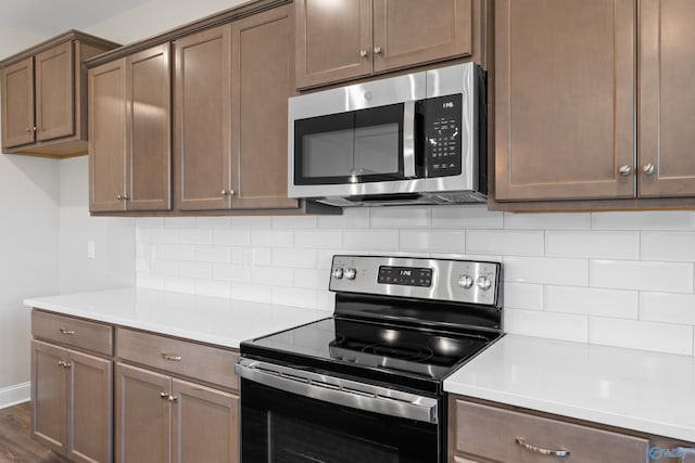 kitchen featuring stainless steel appliances, dark wood-style flooring, light countertops, and decorative backsplash