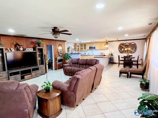 tiled living room featuring ceiling fan with notable chandelier, wood walls, and crown molding