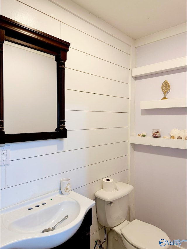 bathroom with vanity, wood walls, and toilet