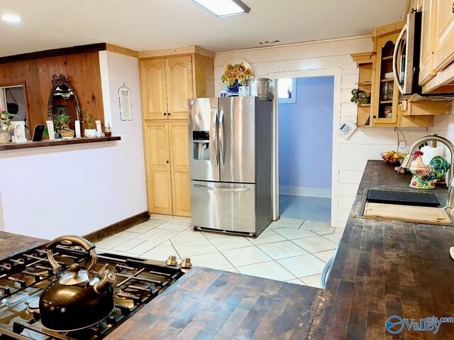 kitchen featuring stainless steel appliances, light brown cabinets, light tile patterned flooring, and wooden walls