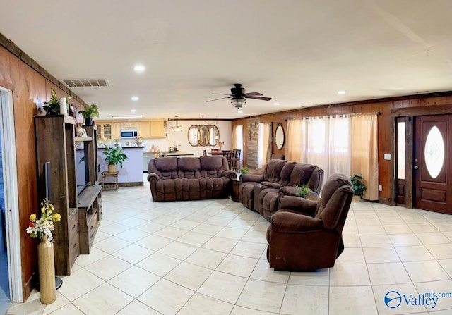 living room featuring light tile patterned floors, wood walls, and ceiling fan