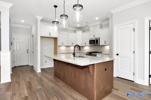 kitchen featuring light stone countertops, white cabinetry, appliances with stainless steel finishes, and a kitchen island with sink