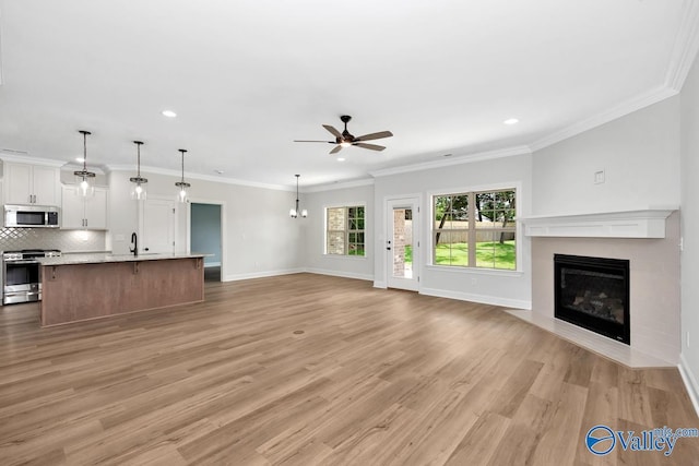 unfurnished living room featuring ornamental molding, sink, ceiling fan, and light wood-type flooring