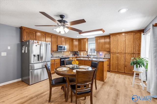 kitchen with decorative backsplash, ceiling fan, a textured ceiling, light wood-type flooring, and stainless steel appliances