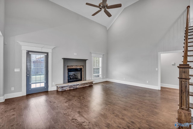 unfurnished living room featuring a stone fireplace, dark hardwood / wood-style floors, high vaulted ceiling, and ceiling fan