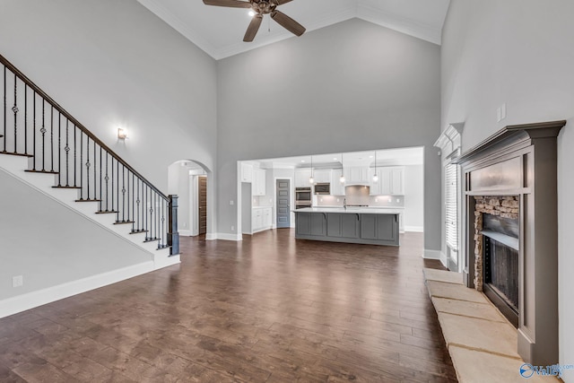 unfurnished living room with ornamental molding, dark wood-type flooring, a high ceiling, and ceiling fan