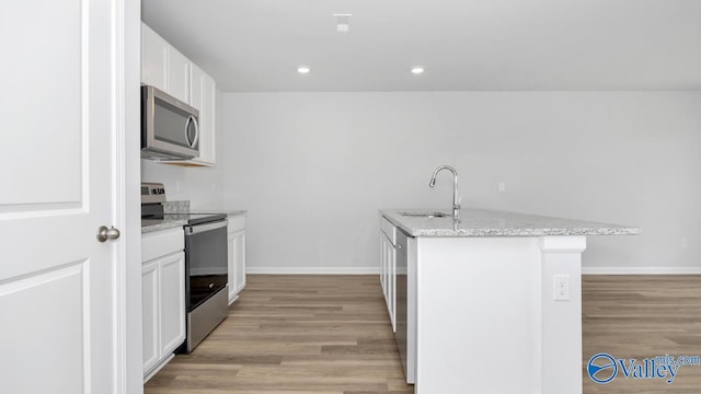 kitchen featuring a sink, a center island with sink, light wood-type flooring, white cabinetry, and appliances with stainless steel finishes