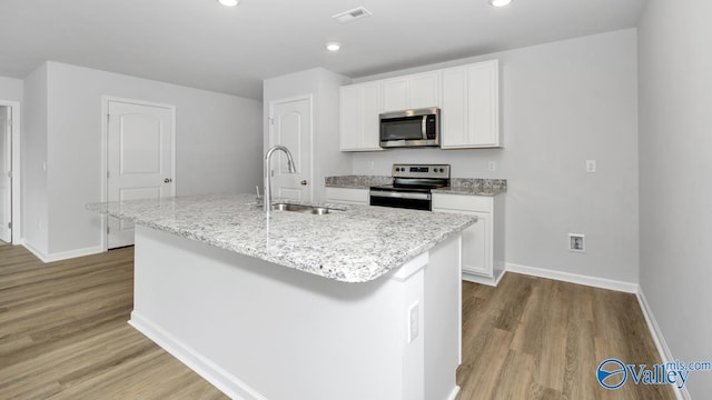 kitchen with an island with sink, stainless steel appliances, light wood-style floors, a sink, and visible vents