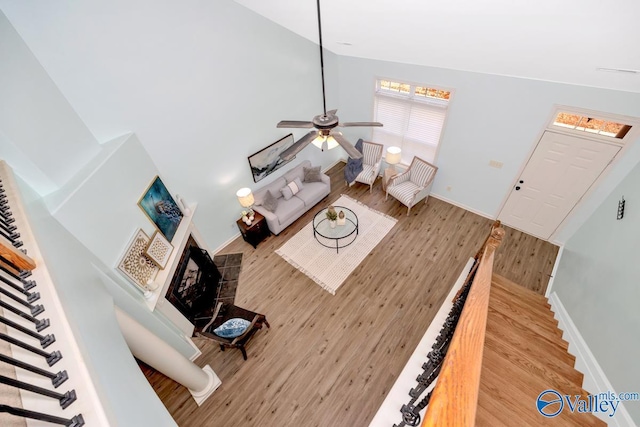 living room with a fireplace with raised hearth, high vaulted ceiling, wood finished floors, baseboards, and stairway