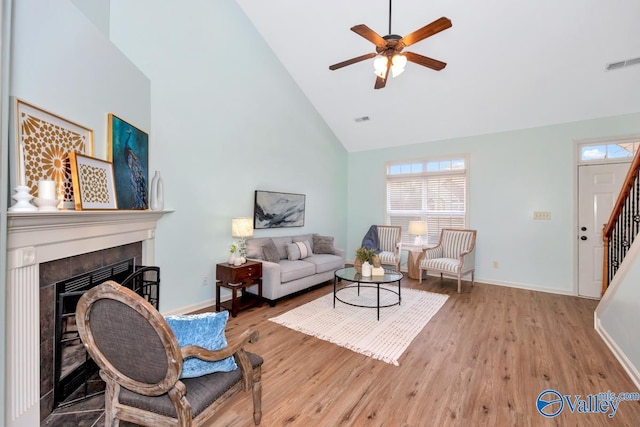 living room with light wood finished floors, visible vents, a tiled fireplace, high vaulted ceiling, and stairs