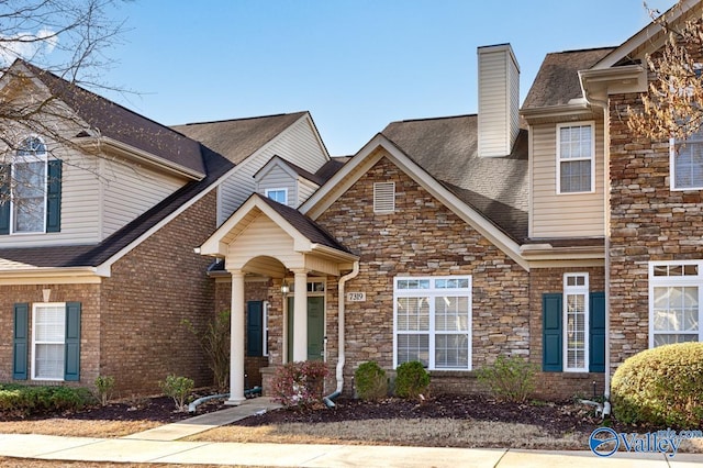 view of front of home featuring a shingled roof, brick siding, and a chimney