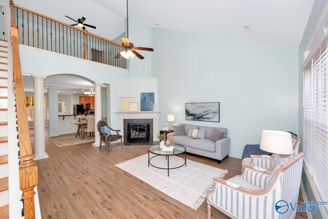 living room featuring a tiled fireplace, light hardwood / wood-style flooring, ceiling fan, and ornate columns