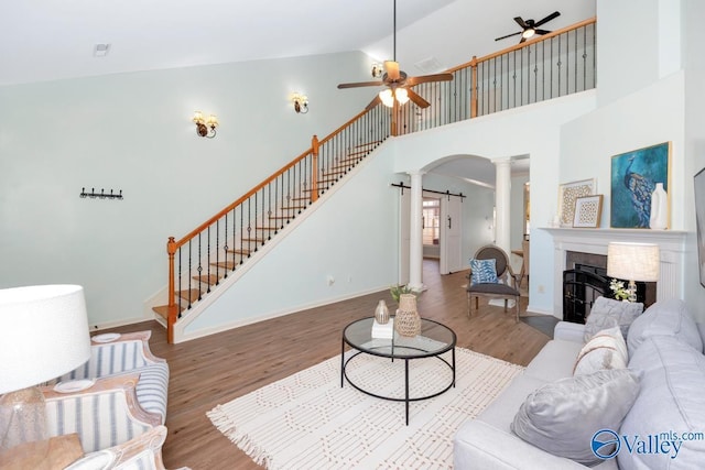 living room with a ceiling fan, a tile fireplace, stairway, wood finished floors, and ornate columns