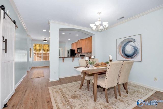 dining space with light wood-style floors, a barn door, visible vents, and crown molding