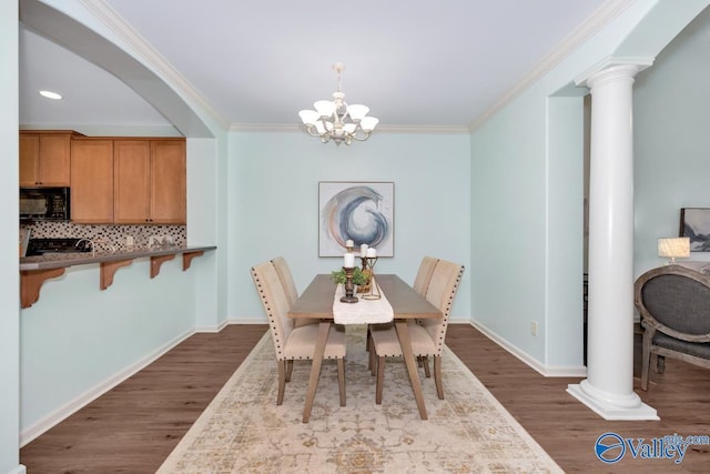 dining room featuring dark wood-style flooring, crown molding, ornate columns, and an inviting chandelier