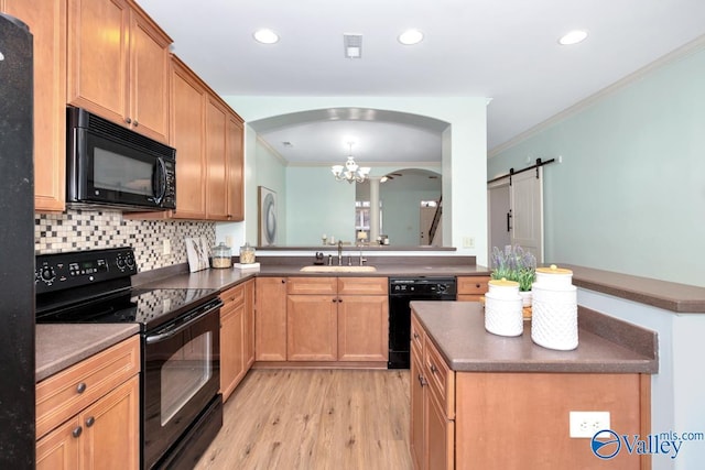 kitchen with black appliances, a barn door, dark countertops, and a sink