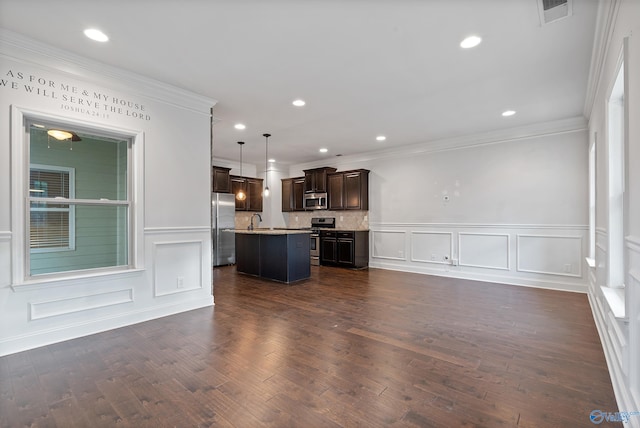 kitchen with appliances with stainless steel finishes, dark hardwood / wood-style floors, decorative light fixtures, and an island with sink