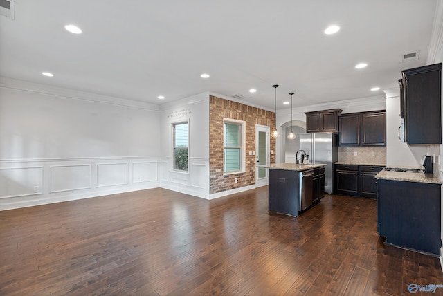 kitchen with dark wood-type flooring, a center island with sink, hanging light fixtures, tasteful backsplash, and appliances with stainless steel finishes