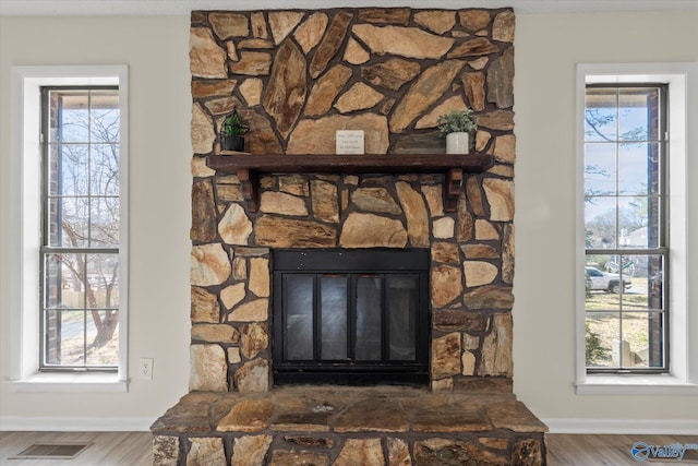 details featuring visible vents, a stone fireplace, baseboards, and wood finished floors