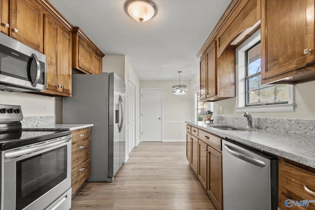 kitchen featuring brown cabinets, light wood-style flooring, stainless steel appliances, and a sink