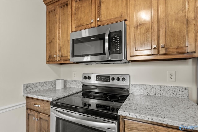 kitchen with appliances with stainless steel finishes, brown cabinetry, and light stone countertops