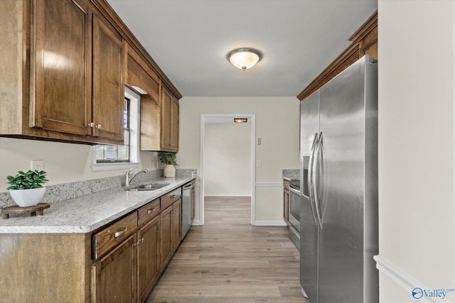 kitchen with light wood finished floors, appliances with stainless steel finishes, a sink, and baseboards