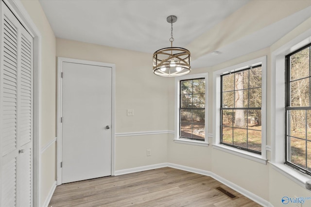 unfurnished dining area with a chandelier, light wood-type flooring, visible vents, and baseboards