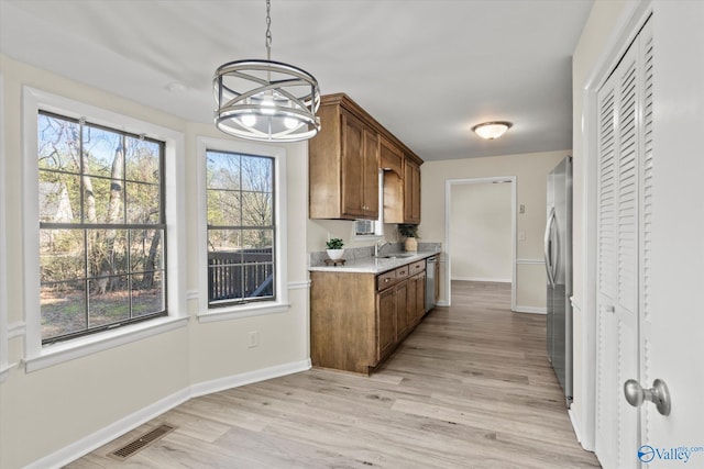 kitchen featuring stainless steel appliances, a sink, visible vents, brown cabinets, and light wood finished floors