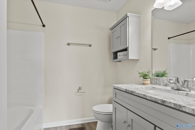 bathroom with toilet, wood finished floors, vanity, baseboards, and shower / washtub combination