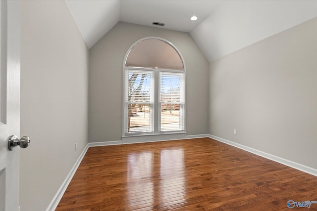 empty room featuring hardwood / wood-style flooring, baseboards, and lofted ceiling