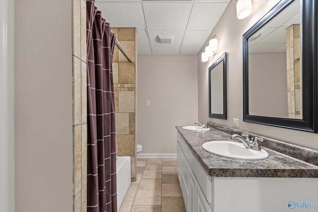 bathroom with double vanity, toilet, a drop ceiling, and a sink