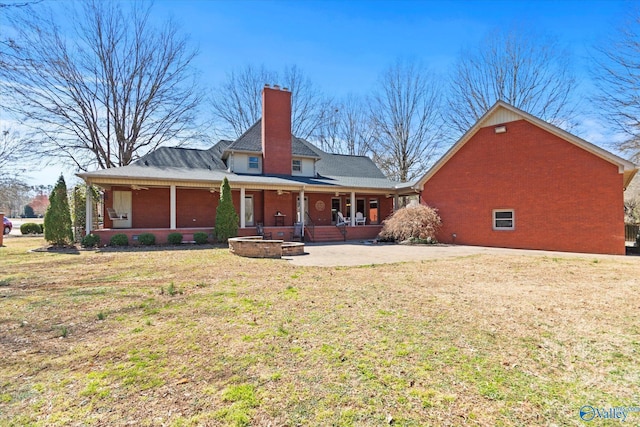 back of property featuring a yard, covered porch, a chimney, a patio area, and brick siding