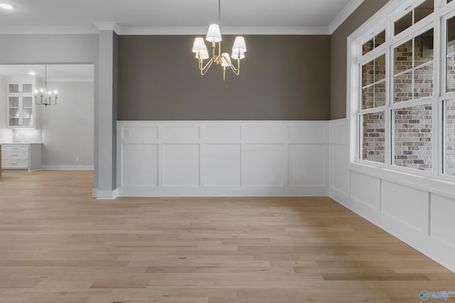 unfurnished dining area featuring ornamental molding, light wood-type flooring, and a notable chandelier